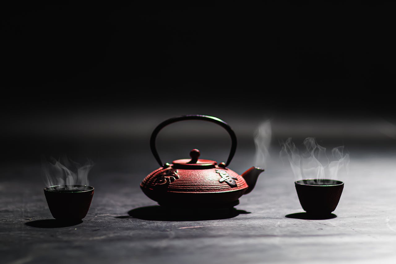 Minimalist image of a cast iron teapot and steaming cups, perfect for traditional tea culture themes.