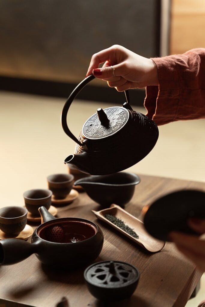 Close-up of a hand pouring tea from a traditional black teapot into cups.
